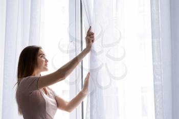Young woman opening curtains in morning�