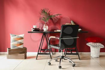 Dark table with comfortable armchair near color wall in room�