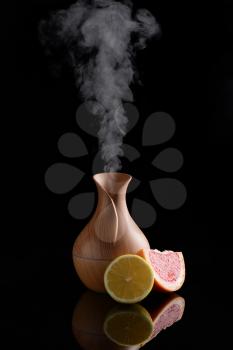Aroma oil diffuser and citrus fruits on dark background�