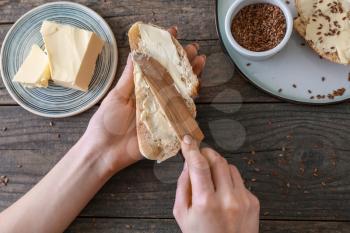 Woman spreading tasty butter onto slice of bread on wooden background�