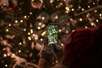 Woman taking picture of beautifully decorated Christmas tree outdoors�