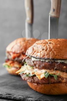 Tasty burgers with knives on grunge background�