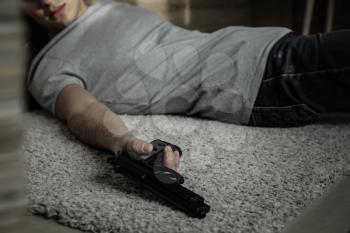 Body of man with gun after committing suicide lying on floor�