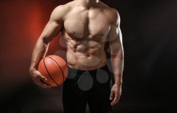 Muscular bodybuilder with ball on dark background 