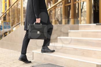 Businessman with stylish briefcase going upstairs outdoors�