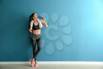 Sporty young woman with bottle of water near color wall�