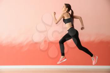 Sporty young woman running against color wall�