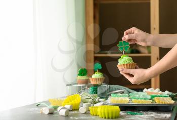 Woman cooking tasty cupcakes for St. Patrick's Day in kitchen�