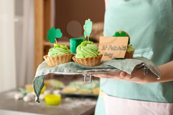 Woman cooking tasty cupcakes for St. Patrick's Day in kitchen�