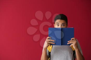 African-American schoolboy with book on color background�