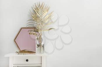 Golden tropical leaves and mirror on table near white wall�