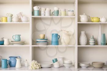 Set of clean dishes on white shelves in kitchen�