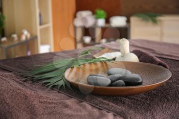 Plate with massage stones on table in spa salon�