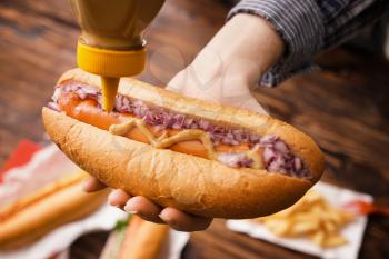 Woman squeezing mustard from bottle onto tasty hot dog, closeup�
