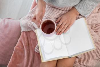Young woman drinking hot tea while reading book at home�