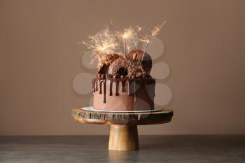 Sweet chocolate cake with sparklers on table against color background�