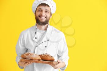 Young baker with fresh bread on color background�
