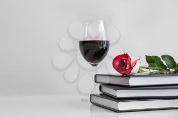 Books, rose flower and glass of wine on table�