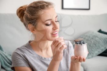 Young woman eating tasty yogurt at home�