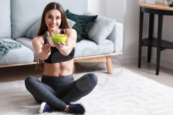 Sporty woman eating tasty yogurt at home�