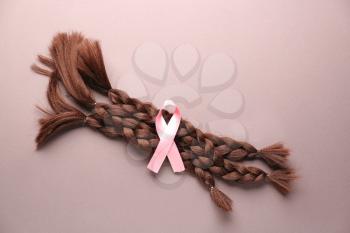 Braided strands and pink ribbon on color background. Concept of hair donation for breast cancer patients�