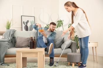 Housewife with brush scolding her lazy husband resting on couch�