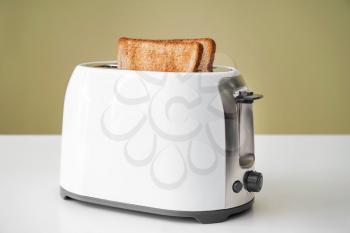 Toaster with bread slices on table against color background�