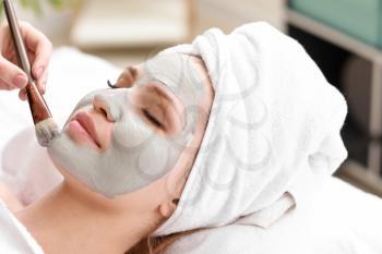 Cosmetologist applying mask onto face of young woman in beauty salon�
