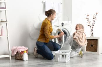 Young woman and her little daughter doing laundry at home�