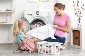 Young woman and her little daughter playing while doing laundry at home�