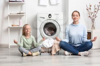 Young woman and her little daughter meditating while doing laundry at home�