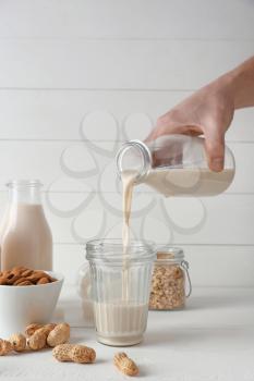 Man pouring tasty vegan milk from bottle into glass on white table�