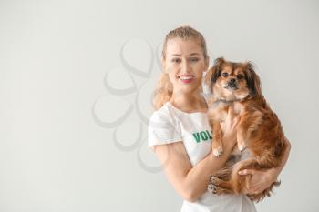 Young female volunteer with dog on light background�