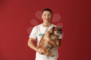 Young male volunteer with dog on color background�