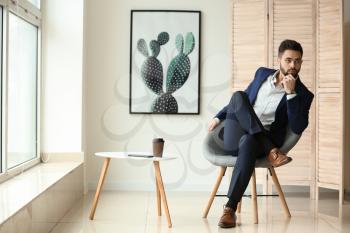 Fashionable young man sitting on chair indoors�