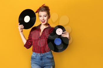 Beautiful pin-up woman with vinyl discs on color background�