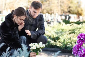 Couple putting flowers on grave of their relative at funeral�