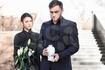 Couple with mortuary urn and flowers at funeral�