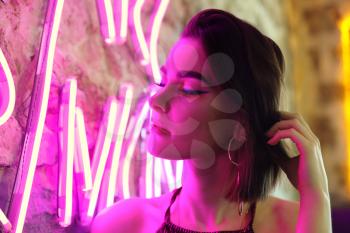 Toned portrait of beautiful young woman near neon lighting on wall�