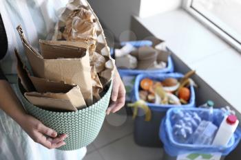 Woman holding trash bin with paper garbage indoors�
