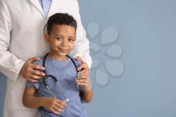 Pediatrician and African-American boy on color background�