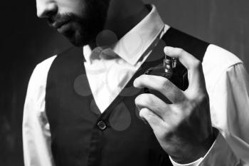 Handsome man with bottle of perfume on grey background, closeup�