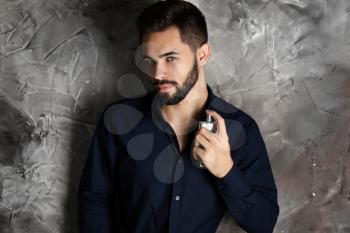 Handsome man with bottle of perfume on grey background�