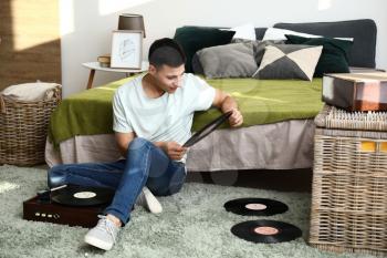 Young man listening to music on record player at home�