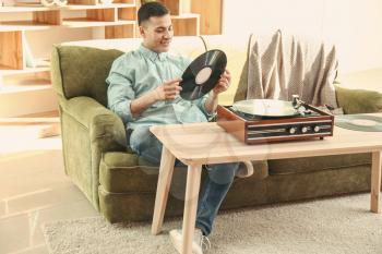 Young man listening to music on record player at home�