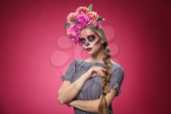 Young woman with painted skull on her face for Mexico's Day of the Dead against color background�