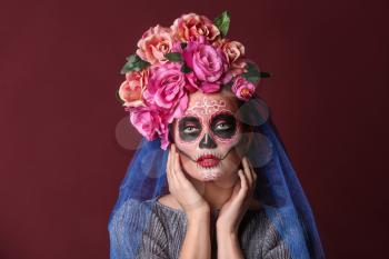 Young woman with painted skull on her face for Mexico's Day of the Dead against color background�