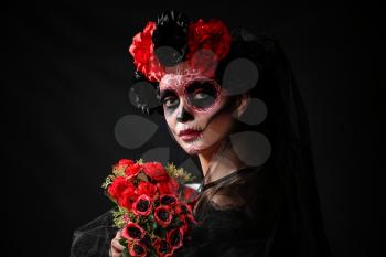 Young woman with painted skull on her face for Mexico's Day of the Dead against dark background�