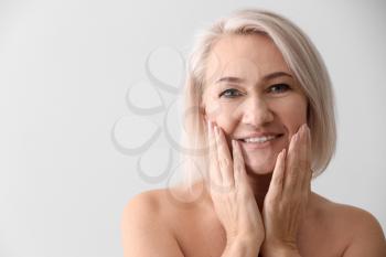 Mature woman giving herself face massage on light background�