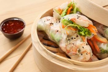 Bamboo steamer with tasty spring rolls on wooden table�